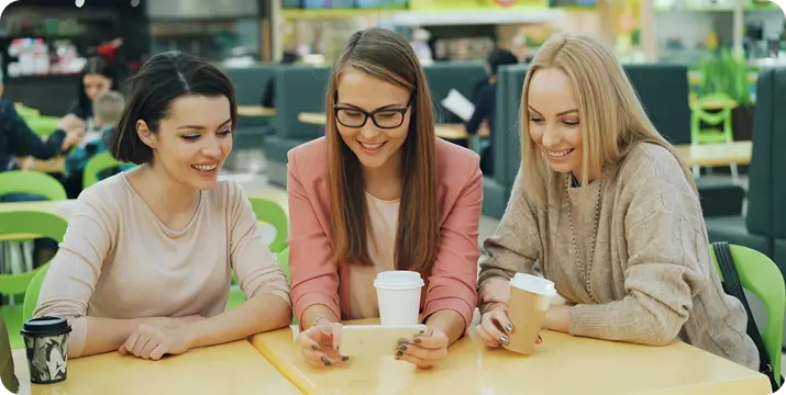 Trois amies souriantes regardant un smartphone autour d'une table