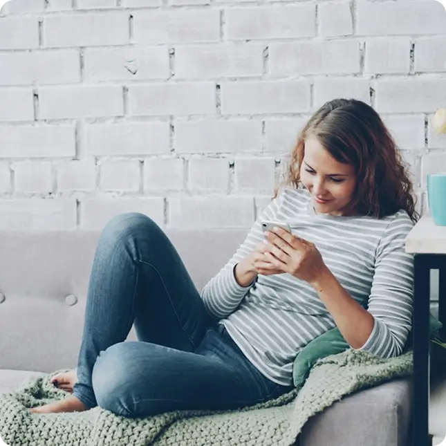 Jeune femme assise sur un canapé consultant son smartphone
