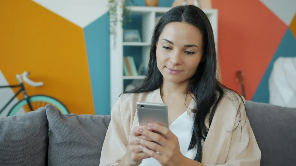 Jeune femme souriante consultant son smartphone sur un canapé